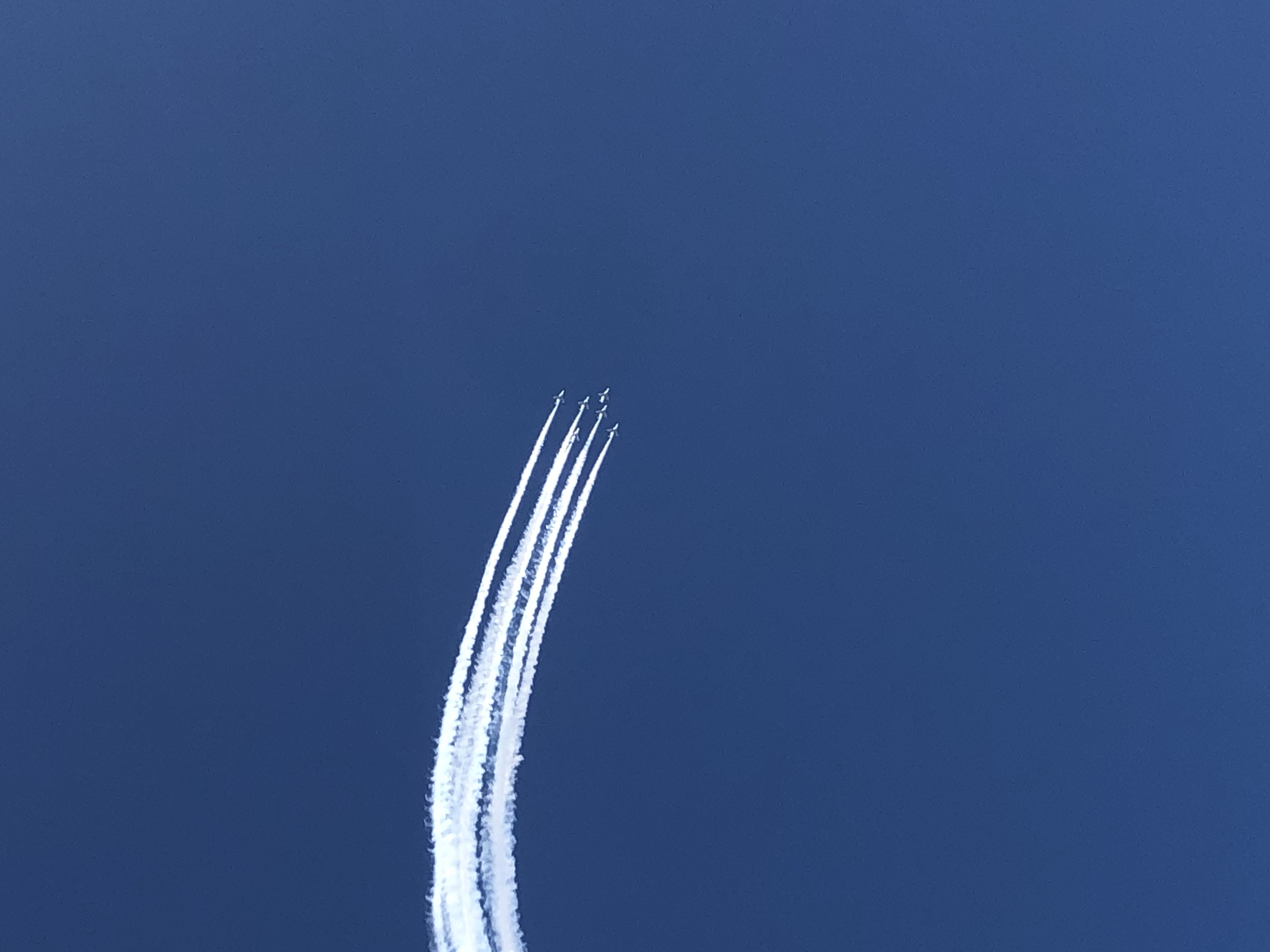 青空に白いスモークの軌跡を描いて旋回するブルーインパルス